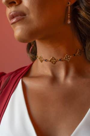 Detalle del cuello de una modelo luciendo el choker dorado Fabiana con piedras azules caladas y pendientes colgantes.