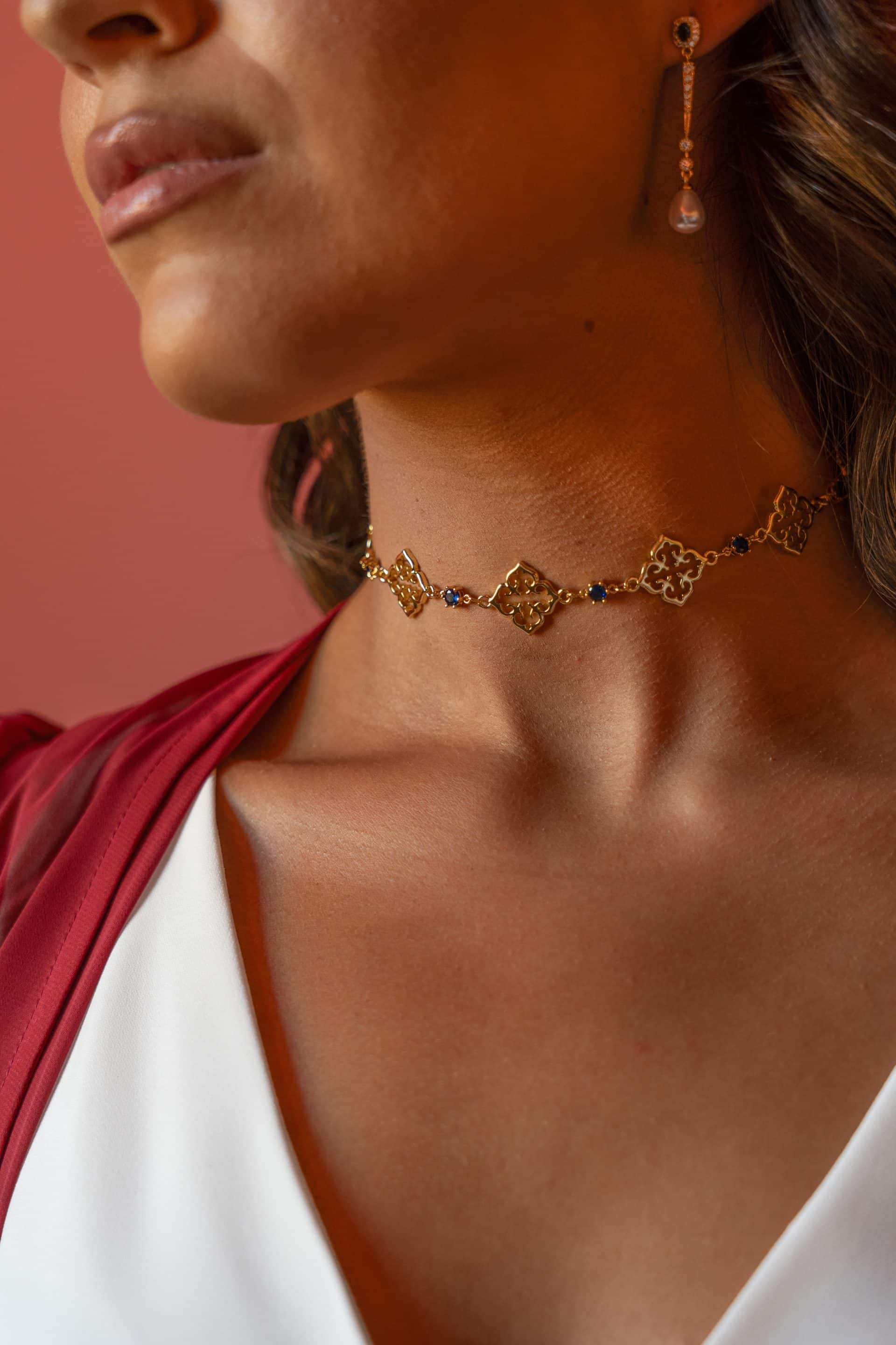 Detalle del cuello de una modelo luciendo el choker dorado Fabiana con piedras azules caladas y pendientes colgantes.