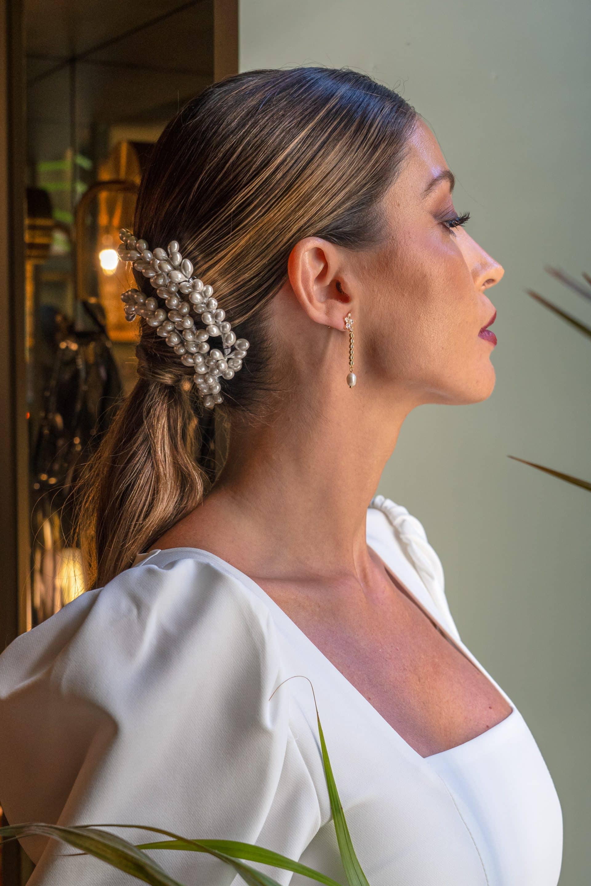 Perfil lateral de una modelo con coleta baja pulida decorada con el tocado de tres hileras de perlas Natalia colocado de lado.