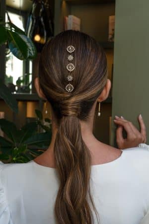 Vista trasera de una modelo con coleta baja decorada con el cubreraiz de cristales Adriana en su versión de solo cresta vertical y con peinecillos laterales.