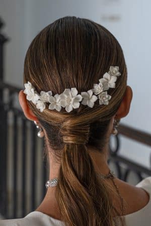 Vista trasera de una modelo con coleta baja decorada con el tocado de flores blancas mate Zaida en forma de arco.