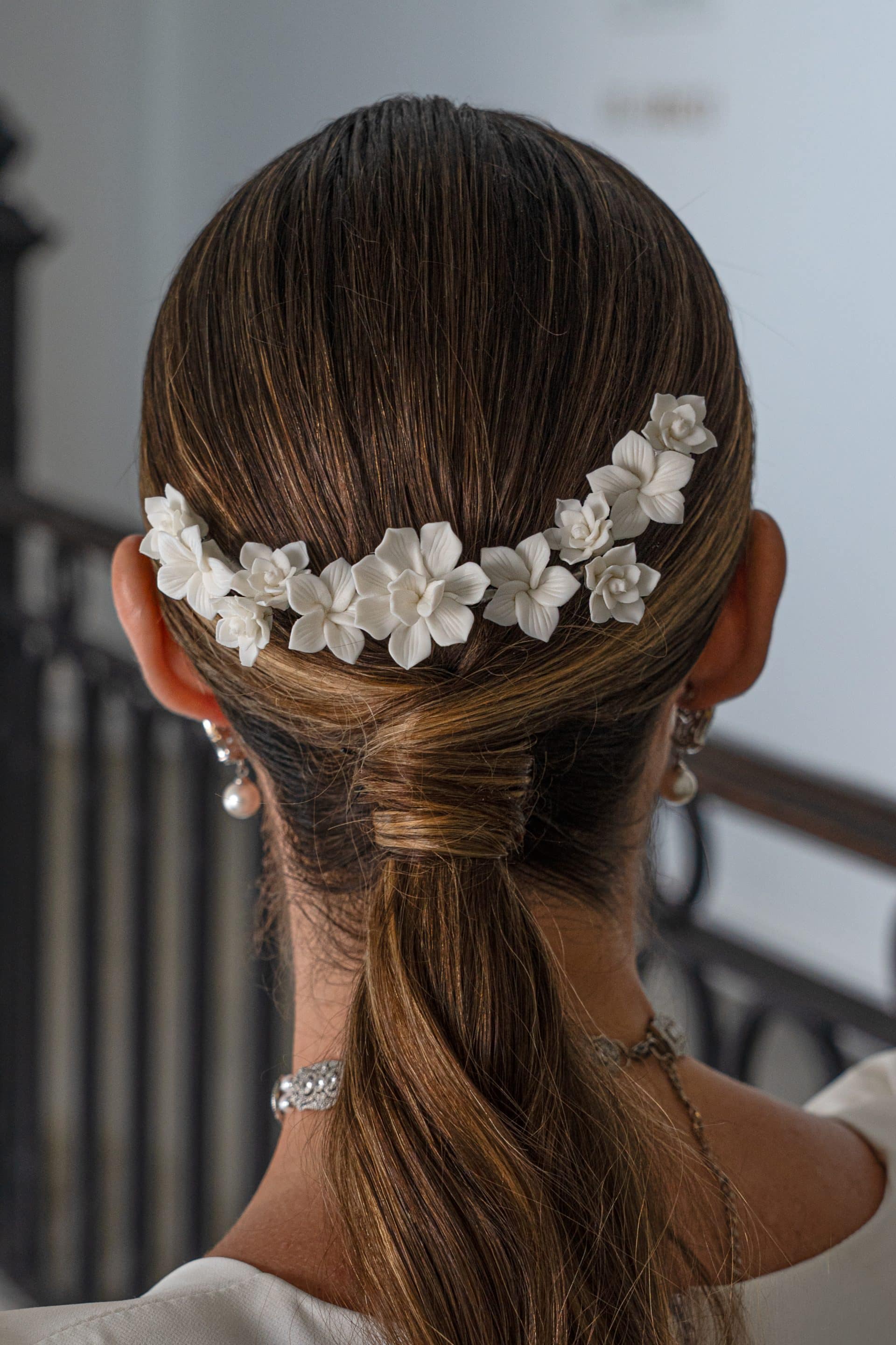 Vista trasera de una modelo con coleta baja decorada con el tocado de flores blancas mate Zaida en forma de arco.
