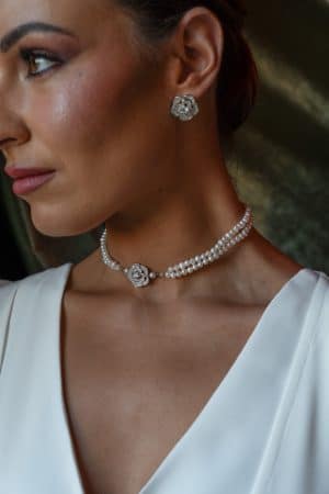 Detalle del cuello de una modelo luciendo el choker de perlas de doble hilera Siena con flor central de cristales y los pendientes a juego.
