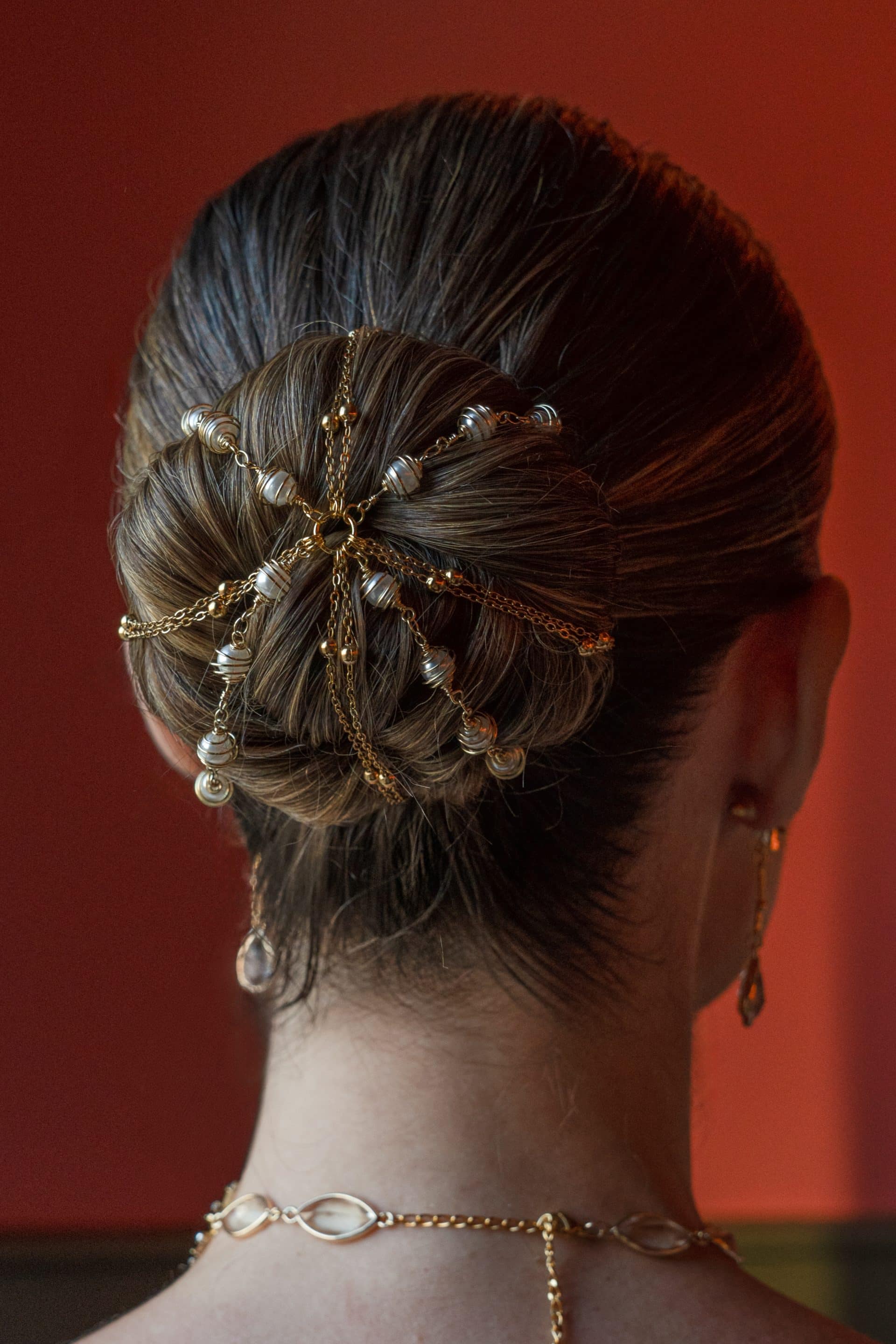 Detalle trasero del moño de una modelo decorado con la red de cadenas doradas y perlas enjauladas del cubremoños Ivet.